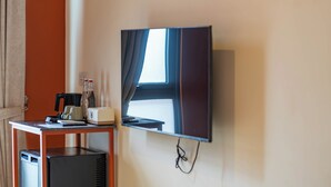 Ein Zimmer mit einem Wand-Fernseher, einem kleinen Tisch mit Kaffeemaschine und einem Minikühlschrank.