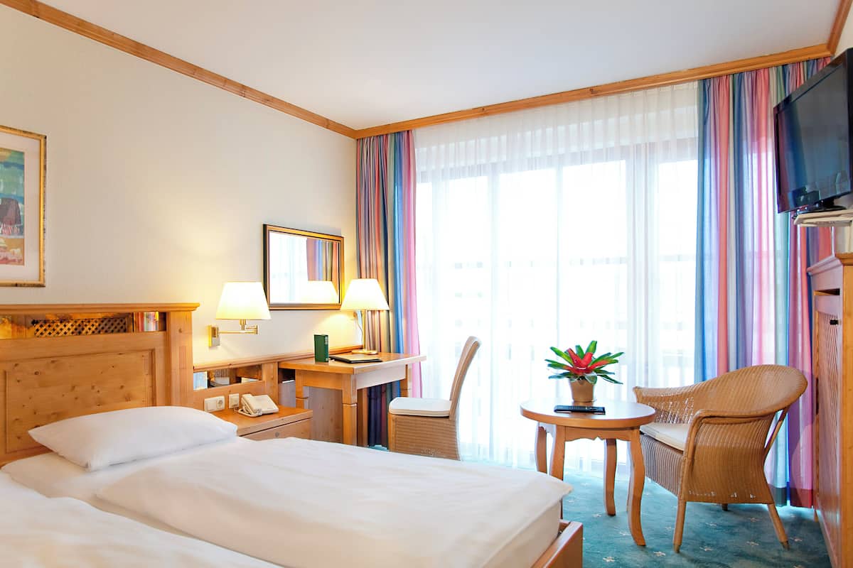 A hotel room with two beds, a desk with a lamp, a chair, a small table with a plant, and a television.