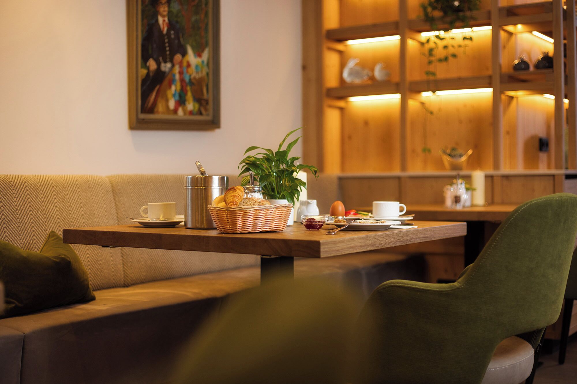 A cozy seating area with a wooden table set for breakfast, including a basket of bread, a croissant, and a coffee cup.