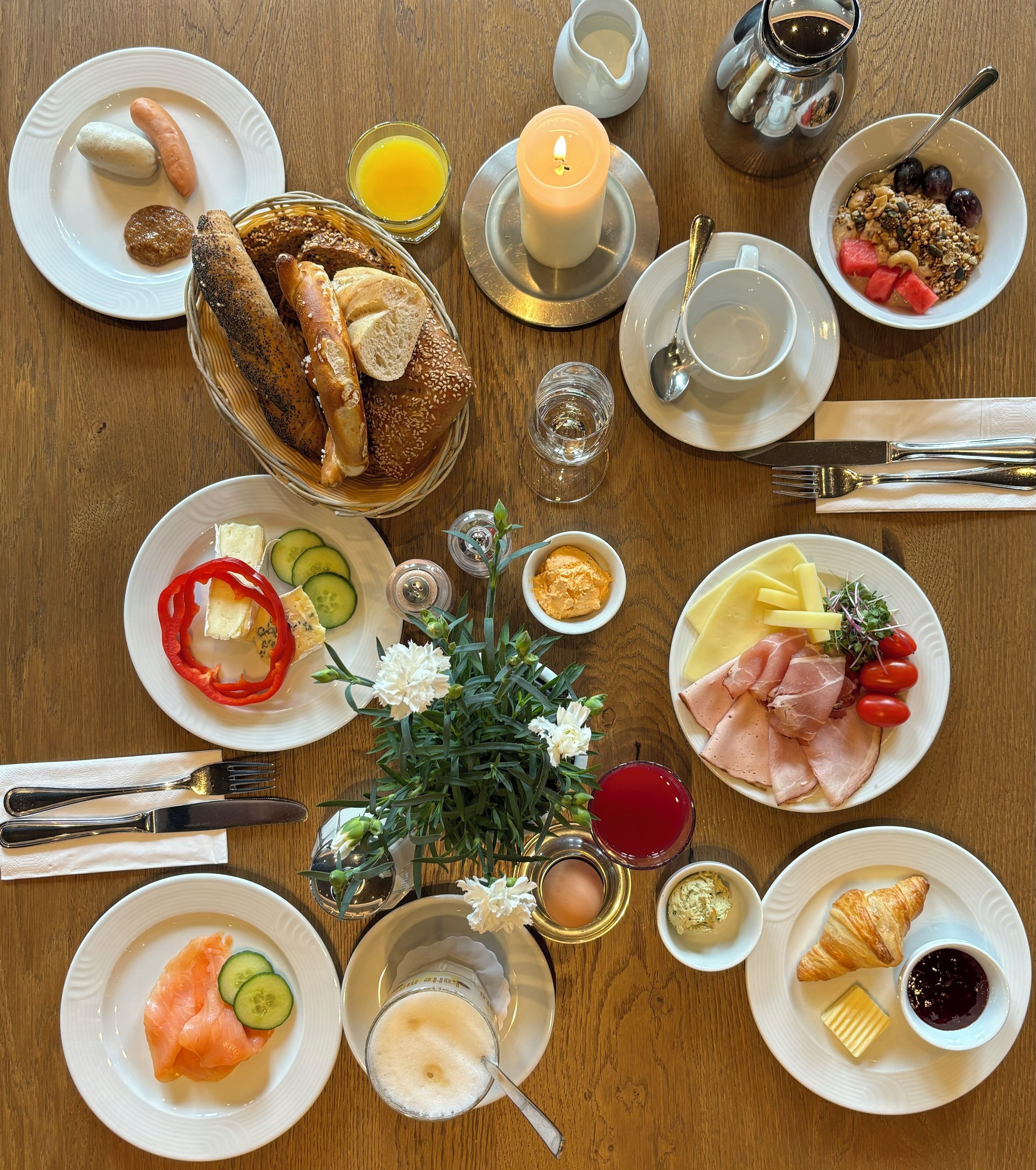 A breakfast setting with various dishes, including bread, eggs, and fruits, arranged on a wooden table.
