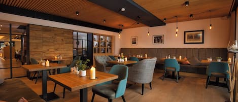 Interior moderno de restaurante con techo de madera, mesas, sillas y zona de estar.