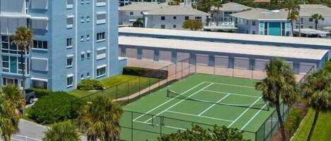 Un edificio de varios pisos con una cancha de tenis al frente.