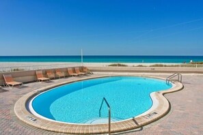 A swimming pool with a curved edge, surrounded by lounge chairs and a view of the beach. - Beachfront Escape at Martinique South: 2BR/2BA Condo (Holmes Beach)
