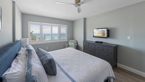 Un dormitorio con una cama, ventilador de techo, televisor, cómoda y una ventana con persianas.