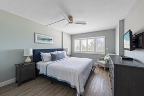A bedroom with a bed, a nightstand, a desk, a chair, a ceiling fan, and a window. - Beachfront Escape at Martinique South: 2BR/2BA Condo (Holmes Beach)