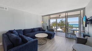 Una sala moderna con un sofá seccional, una mesa redonda y vista al océano a través de puertas de cristal amplias.