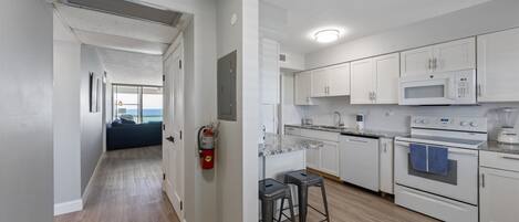 Een moderne keuken met witte kasten, een magnetron, een oven en een inbouw eiland met krukken.
