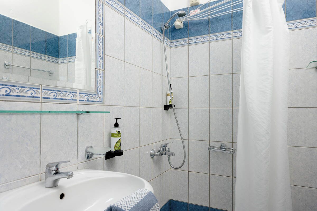 Un baño con lavamanos blanco, ducha con repisa de vidrio y espejo con azulejos decorativos.