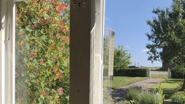 A view through a glass door to an outdoor patio area with a table and chairs, a garden path, and a thermometer indicating a temperature of 20 degrees. - Charming and spacious villa near Lidköping |SE08085 (Lidköping)