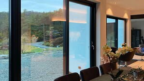 Un comedor moderno con una gran mesa, sillas y vistas a un paisaje natural a través de amplios ventanales.