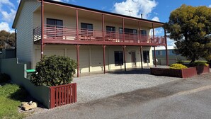 A two-story building with a balcony, a covered entrance, and a gravel driveway.