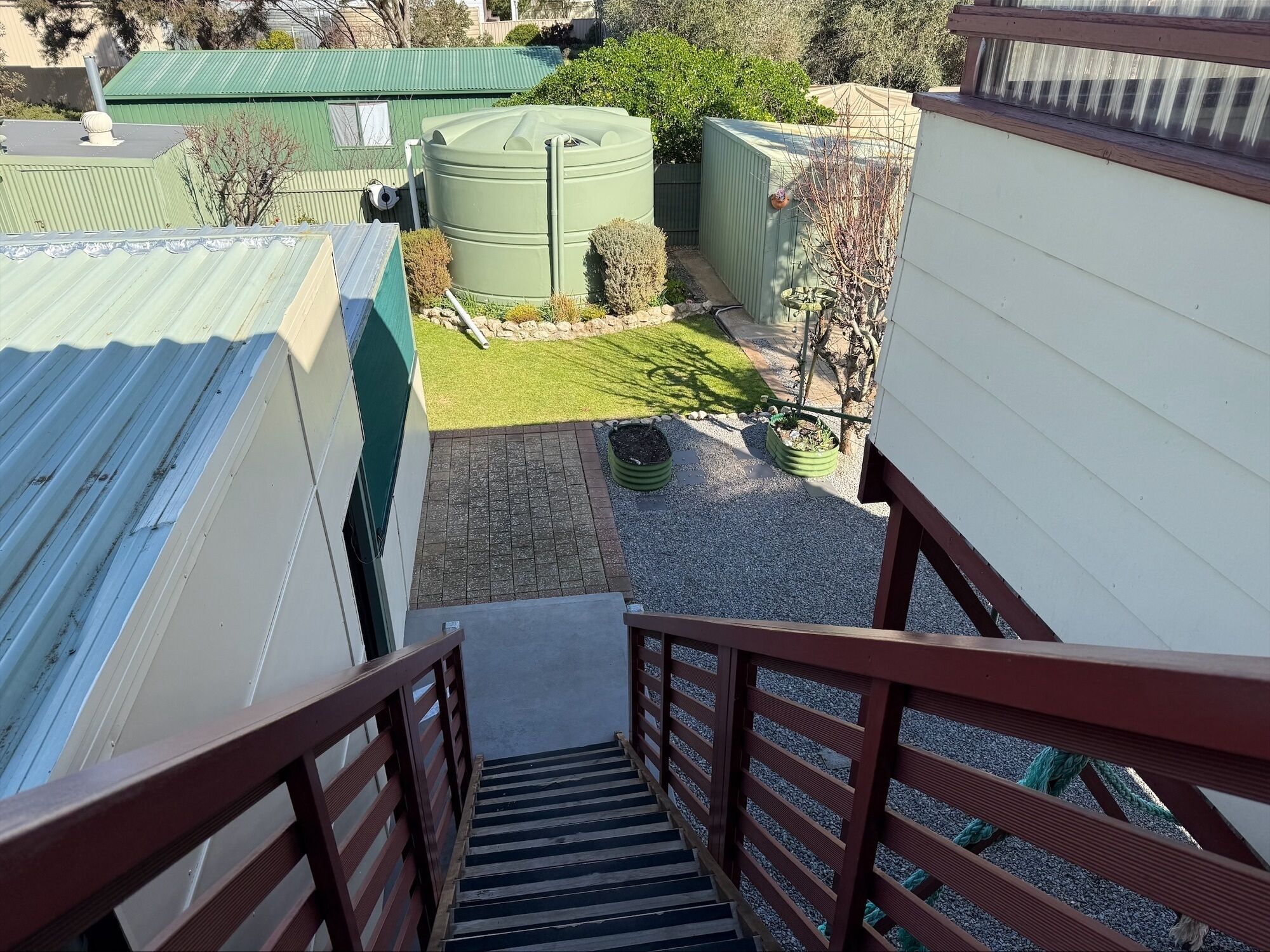 A staircase leading to a rooftop area with a green water tank, a small garden, and a white building.