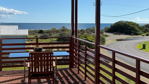 A balcony with a view of the sea, a table, and a chair.