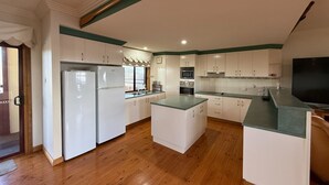 A spacious kitchen with white cabinets, a wooden floor, and a green countertop.