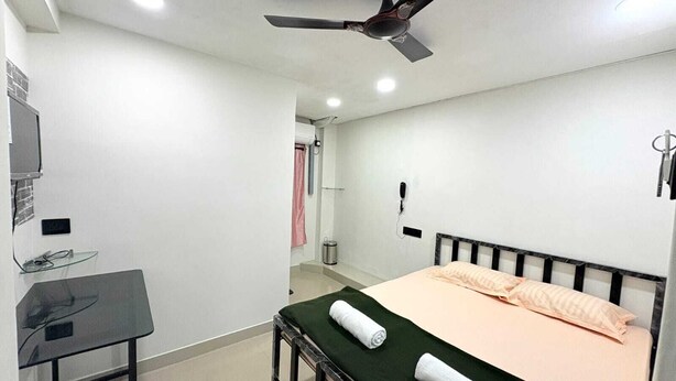 A bedroom with a bed, a desk, a ceiling fan, and a shower area. - Mama Lodging and Boarding (Margao)
