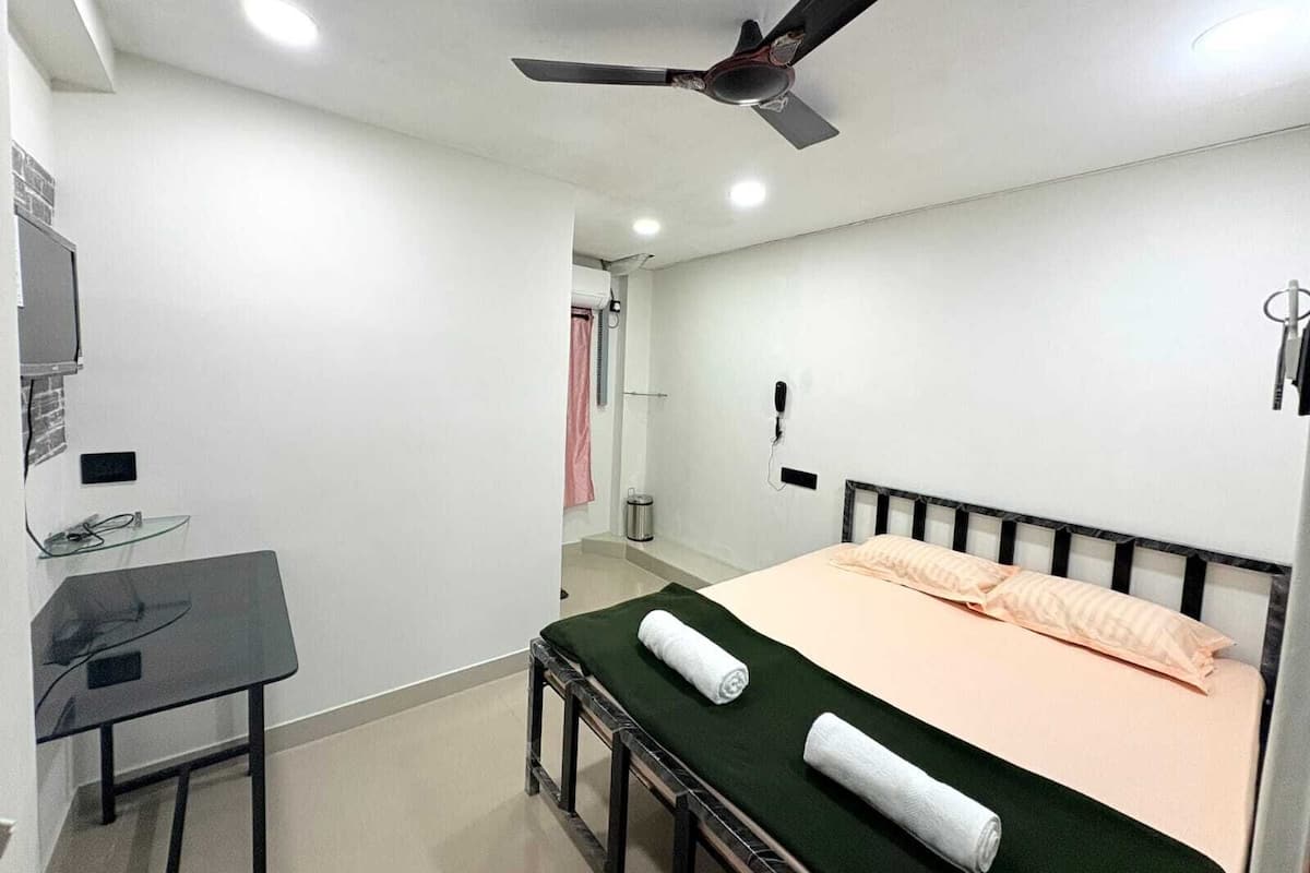 A bedroom with a bed, a desk, a ceiling fan, and a shower area.