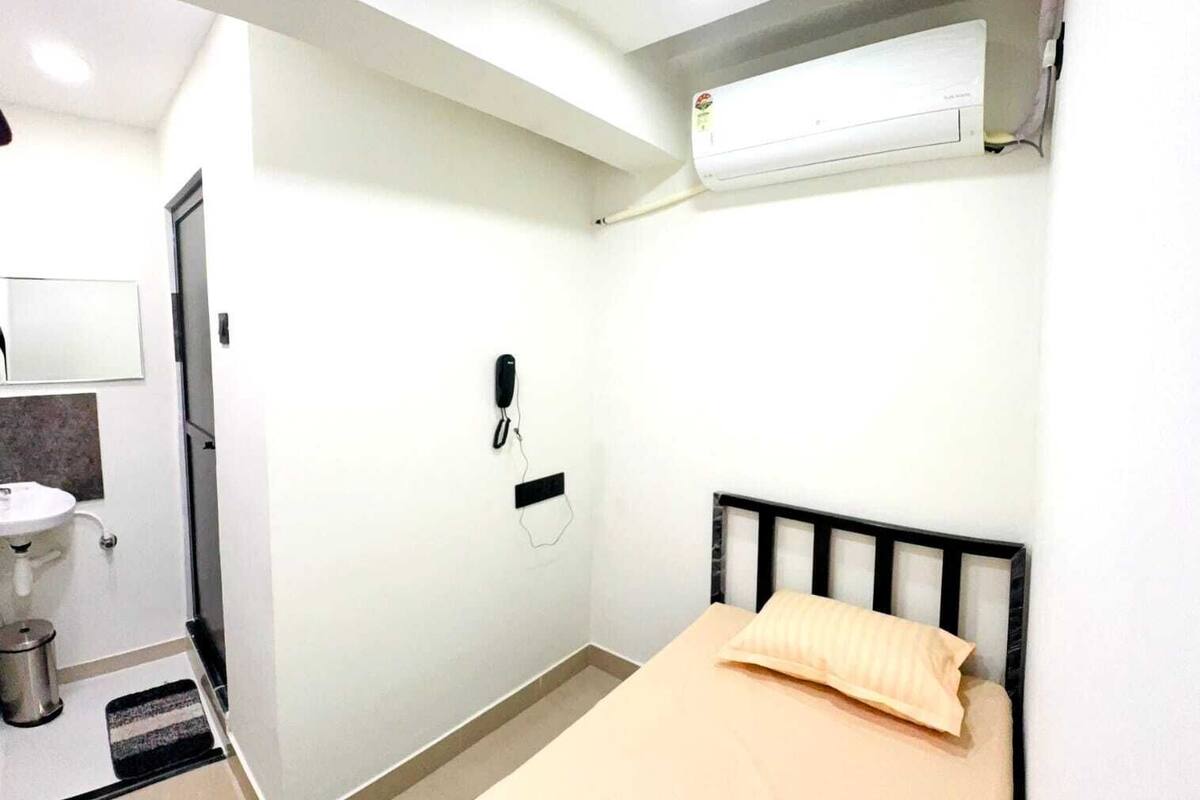 A small, clean room with a bed, a ceiling fan, an air conditioner, a phone, and a sink.