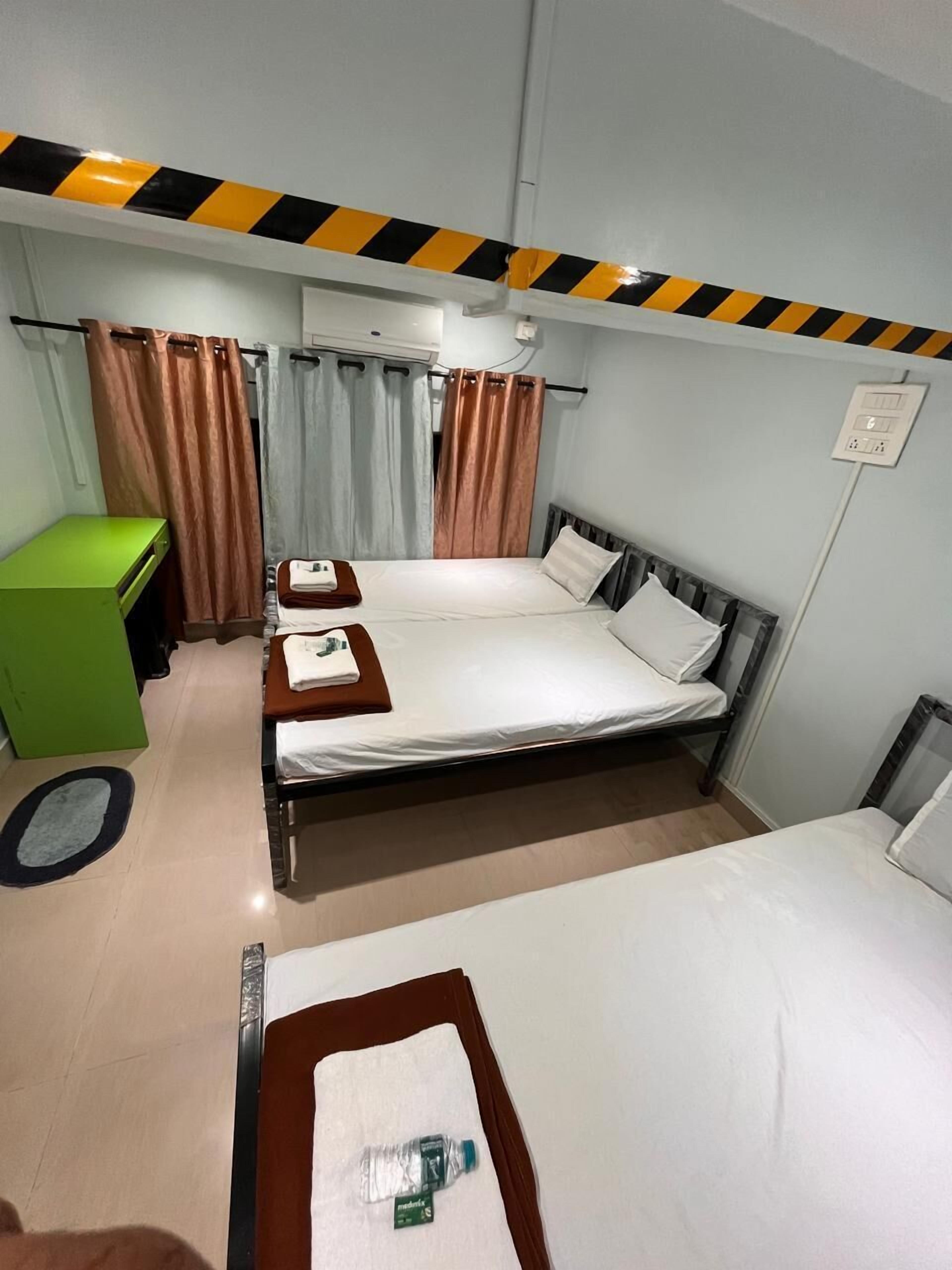 A hotel room with two beds, a green desk, a bathroom, and a shower area.