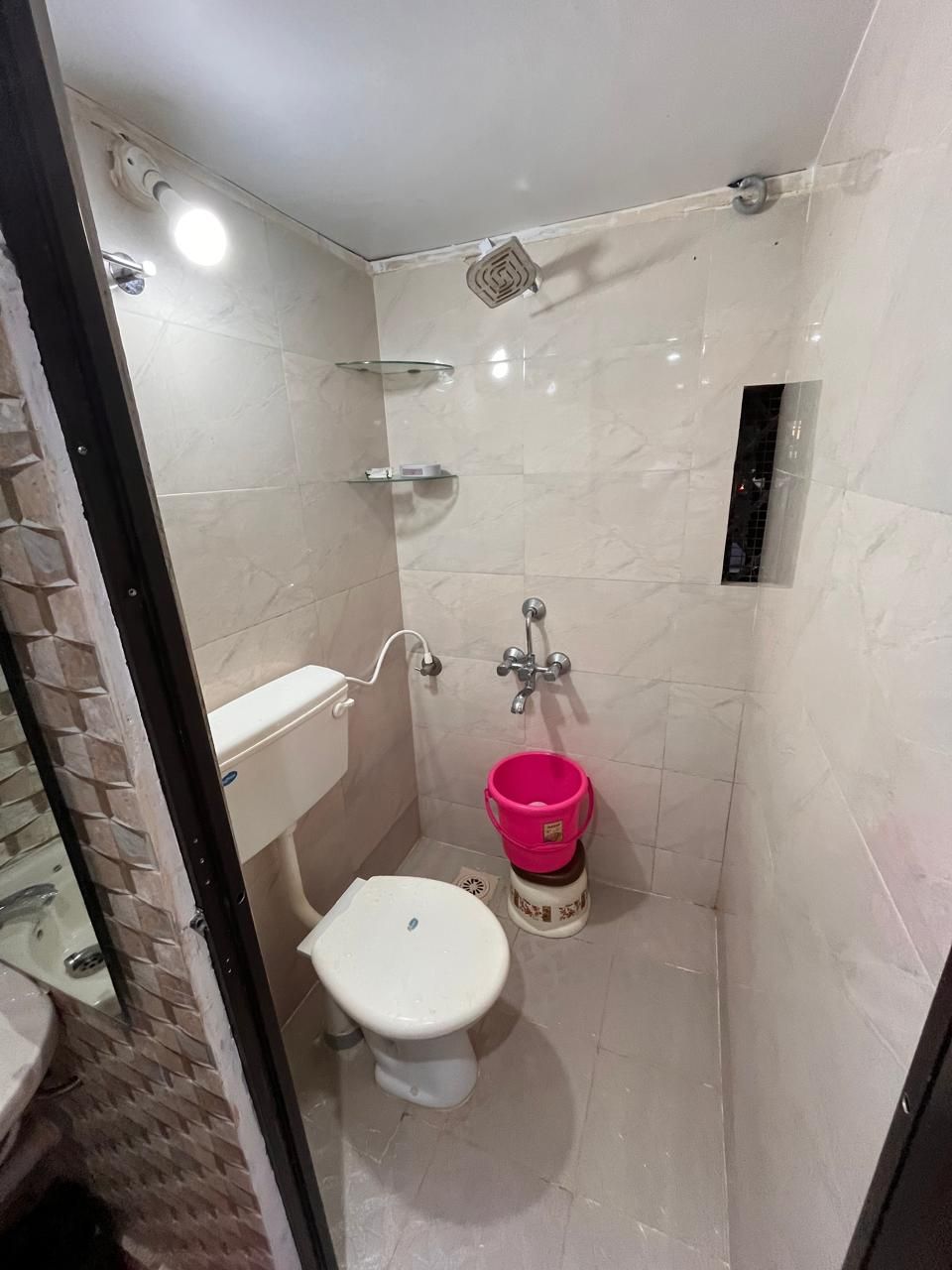 A small, tiled bathroom with a toilet, a shower area, and a glass shelf.