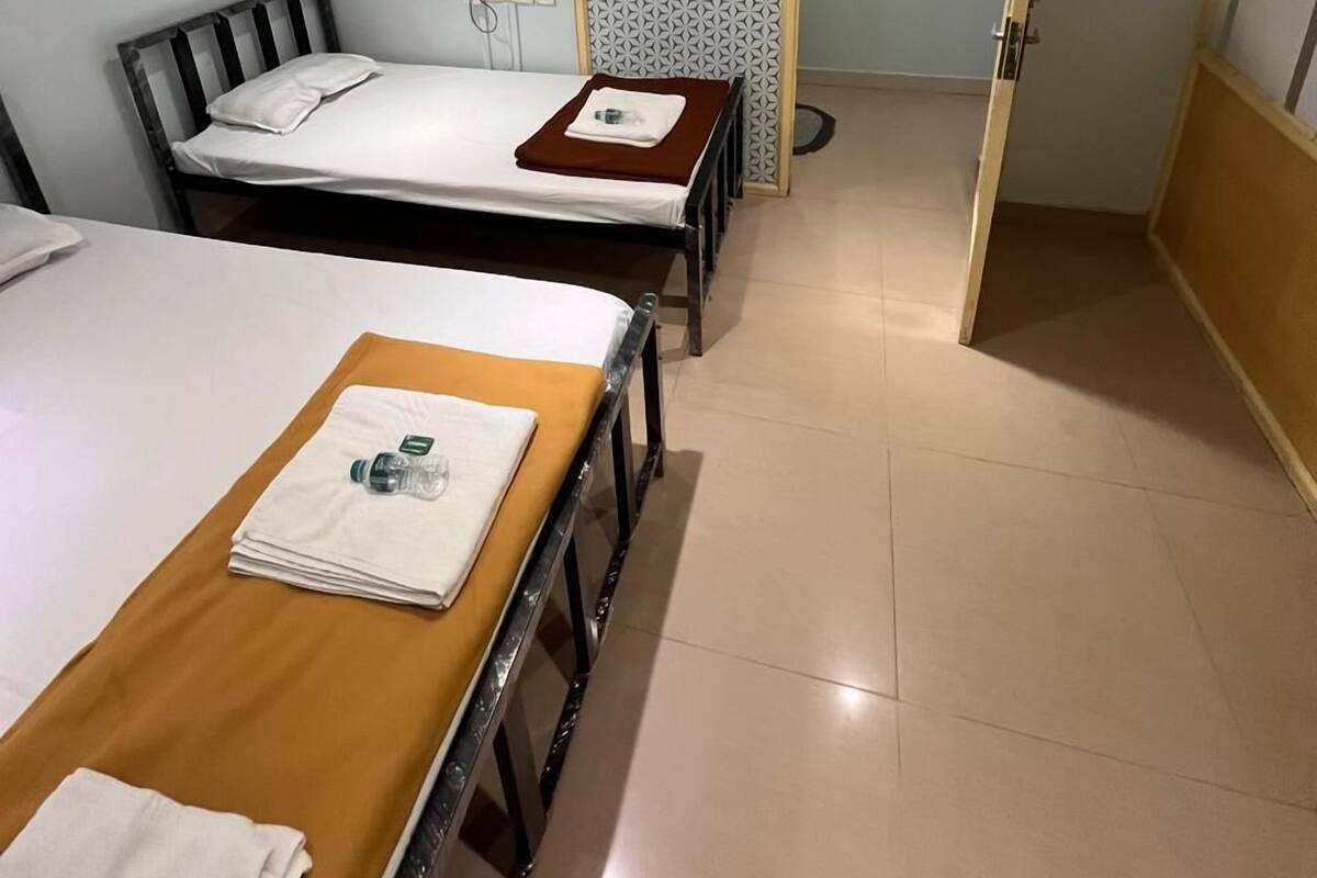A hotel room with two single beds, a wooden table, a small fan, and a patterned door.