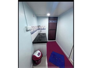 A narrow hallway with a red carpet, a white trash bin, a blue mat, and a sign indicating a wash room. - Mama Lodging and Boarding (Margao)