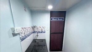 A narrow hallway with a red carpet, a white trash bin, a blue mat, and a sign indicating a wash room. - Mama Lodging and Boarding (Margao)