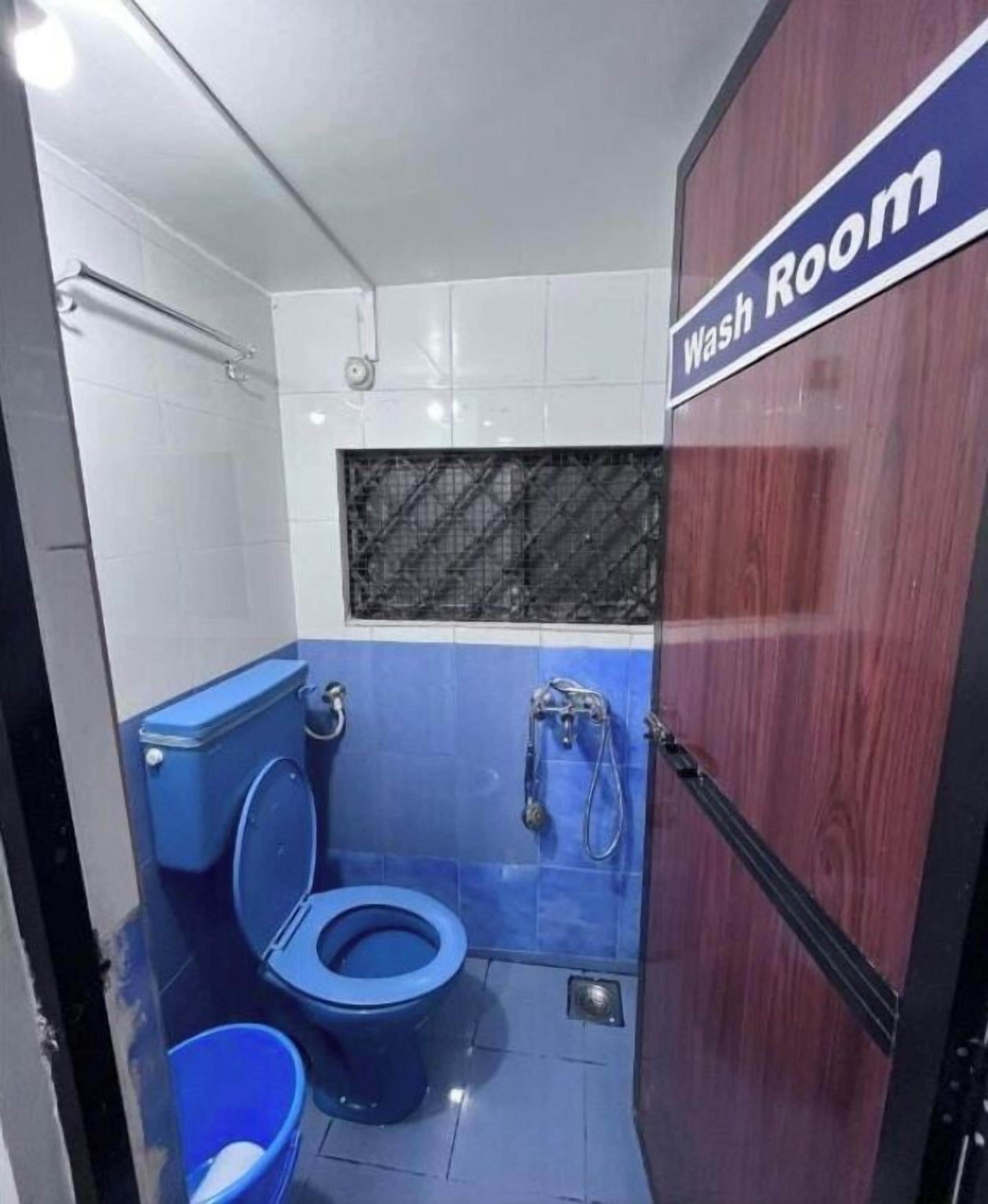 Uma casa de banho pequena e compacta, com sanita azul, zona de duche e porta de madeira.