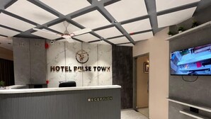 A hotel reception area with a reception desk labeled "RECEPTION" and a wall-mounted clock. - Hotel Pulse Town (Ahmedabad)