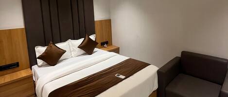 Une chambre d’hôtel moderne avec un grand lit, une table de chevet, une chaise et un ventilateur de plafond.
