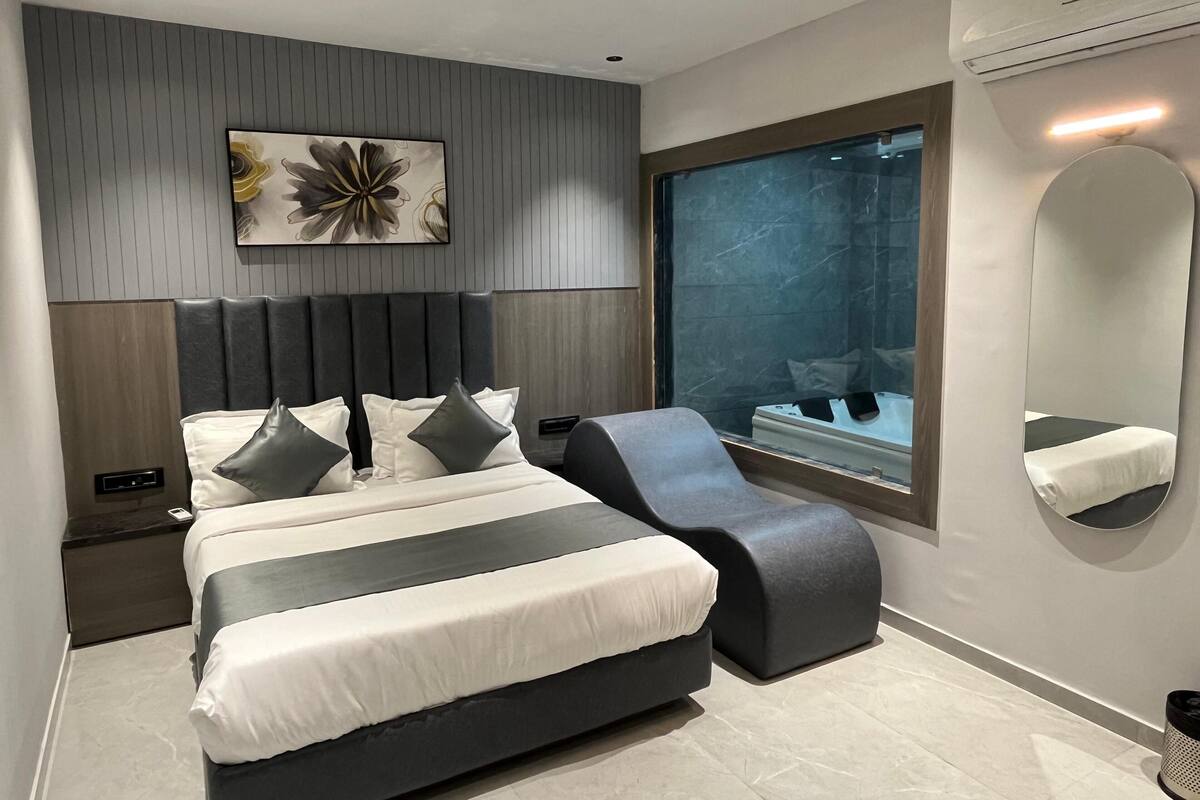 A modern bedroom with a large bed, a curved bench, a large mirror, and a view of a bathroom.