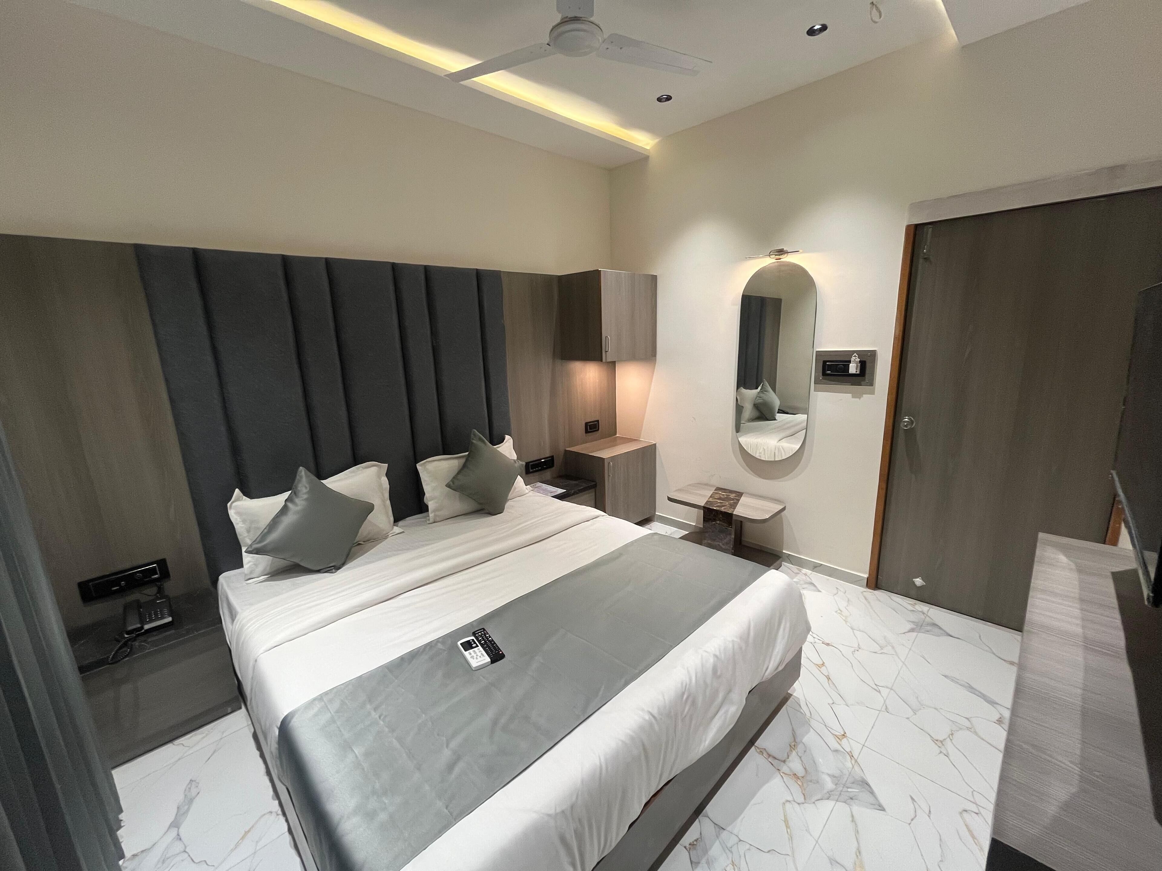 Een moderne hotelkamer met een groot bed, nachtkastjes, een kaptafel met spiegel en een plafondventilator.