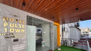 A hotel entrance with a marble facade, a glass door, and a green artificial turf area. - Hotel Pulse Town (Ahmedabad)