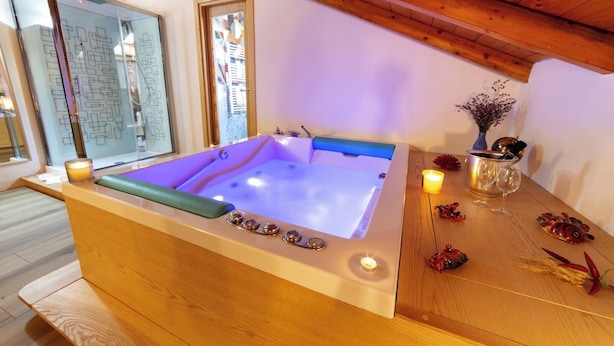 A spa room with a wooden bench, a large bathtub, and a wooden table with candles and decorative items. - La Torre del Nostromo (Salerno)