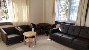 A modern living room with a black leather sofa, two black armchairs, a wooden coffee table, and a small round table. - Brindavan Service Apartments (Mysore)