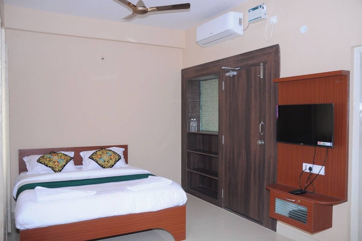 A bedroom with a bed, a wardrobe, a television, and an air conditioning unit.
