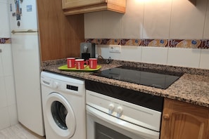 A kitchen with a washing machine, a stove, and a coffee maker.