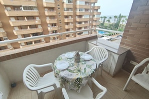 A balcony with a round table set for two, surrounded by white plastic chairs.