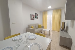 A living room with a sofa, a dining table set with plates and glasses, and a TV on a stand.