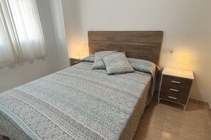 Een slaapkamer met een bed, twee nachtkastjes met lampen en een raam met gordijnen.