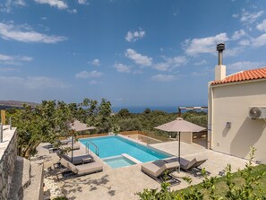 A swimming pool with lounge chairs and umbrellas, surrounded by greenery and a view of the sea. - Athos Rural villa, private pool,a short walk to taverns (Prines)