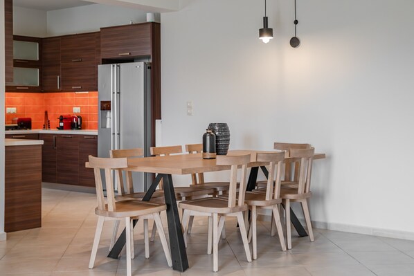 A modern kitchen with wooden cabinets, a stainless steel refrigerator, and a dining table with chairs. - Athos Rural villa, private pool,a short walk to taverns (Prines)