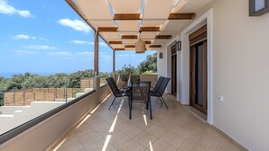 A balcony with a table and chairs, a view of the sea, and a wooden ceiling structure. - Athos Rural Villa (Rethymno)