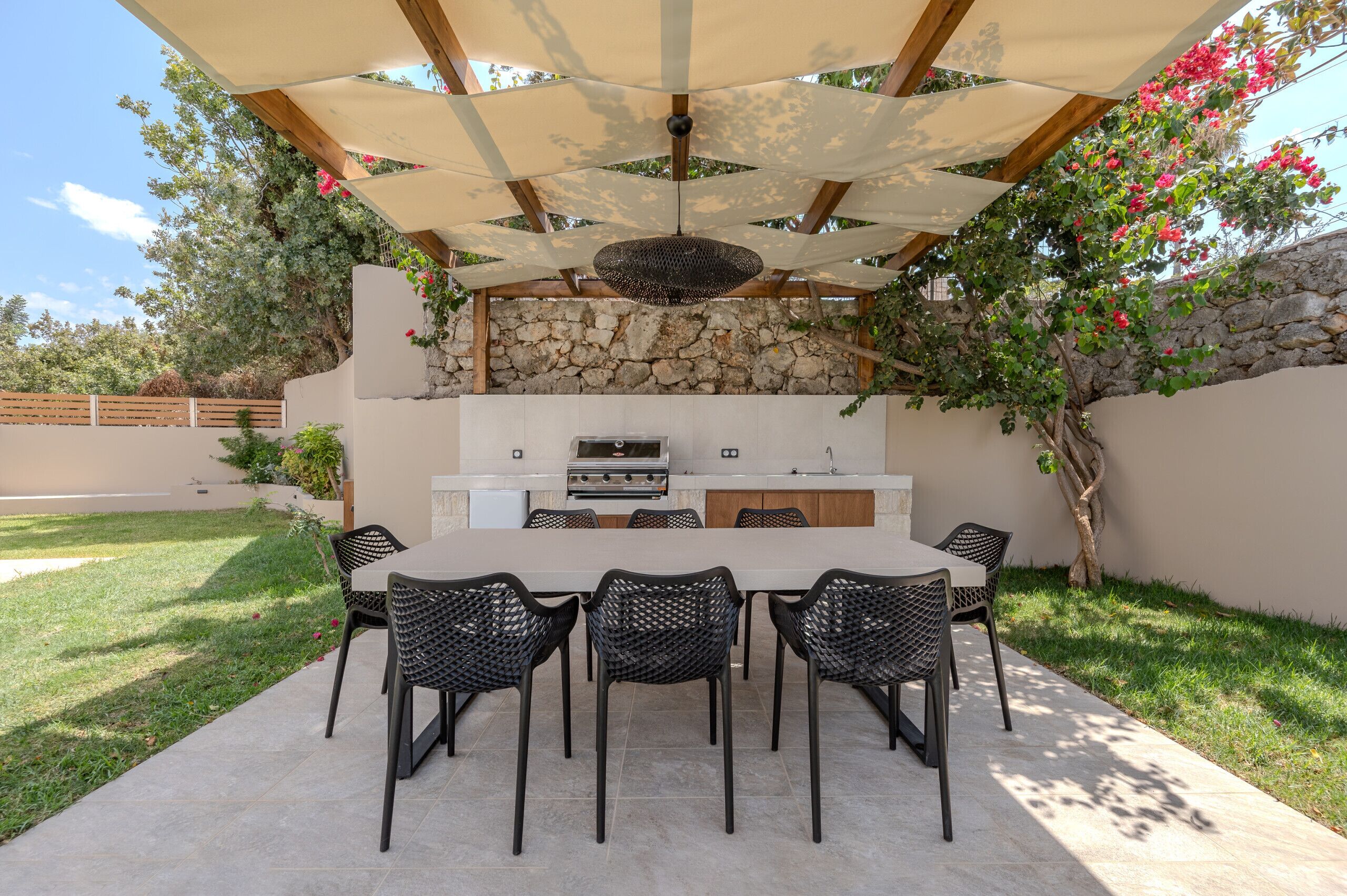 Une cuisine extérieure avec un mur en pierre en arrière-plan, une table à manger avec des chaises et une pergola au-dessus.