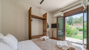 A hotel room with a bed, a wooden wardrobe, a TV, and a view of greenery outside. - Athos Rural Villa (Rethymno)
