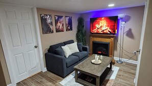 A living room with a fireplace, a sofa, a coffee table, and a television. - Modern 2BR Basement Suite with Jacuzzi  Access, Full Kitchen & Free Wifi (Roosevelt)