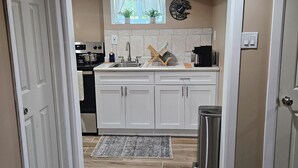 A kitchen with white cabinets, a stainless steel sink, a coffee maker, and a trash can. - Modern 2BR Basement Suite with Jacuzzi  Access, Full Kitchen & Free Wifi (Roosevelt)