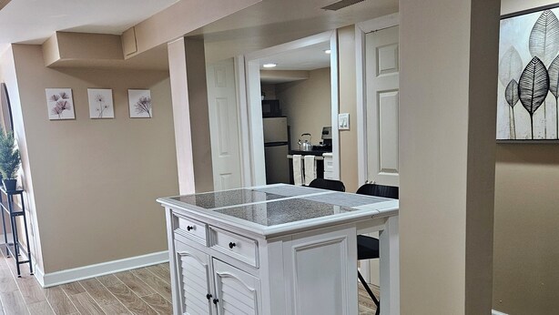 A kitchen with a white island, wooden flooring, and a view into the dining area. - Modern 2BR Basement Suite with Jacuzzi  Access, Full Kitchen & Free Wifi (Roosevelt)