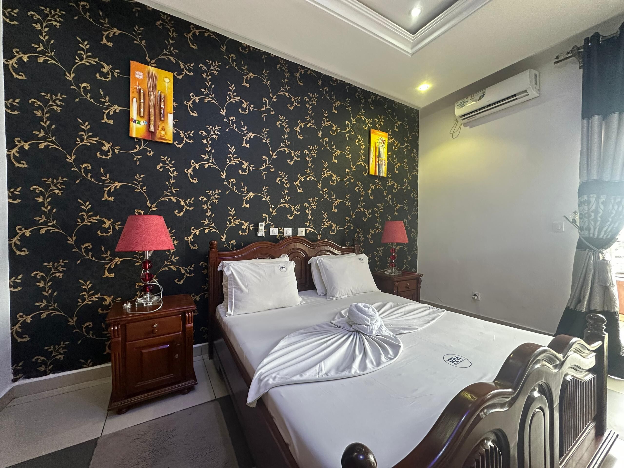 A hotel room with a bed, two bedside tables, lamps, a wall air conditioner, and a window with curtains.