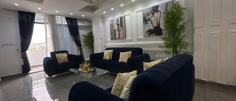 A modern living room with dark blue sofas, a glass coffee table, and a large window with curtains.