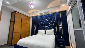 A modern bedroom with a bed, a wardrobe, and a vanity with a mirror. - Tchinda Meli Residence (Douala)